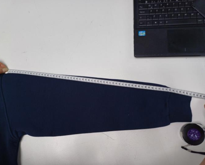 Garment quality inspection measuring the sleeve length of a hoodie using a measurement tape to verify dimensions
