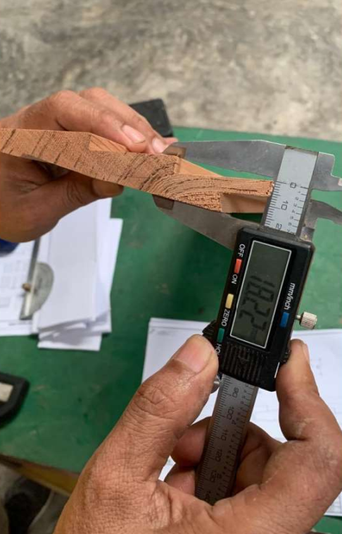 Quality inspection measuring the thickness of a wooden board using a digital caliper during on-site inspection